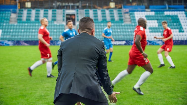 View from behind of a football manager yelling at players on the pitch during a match