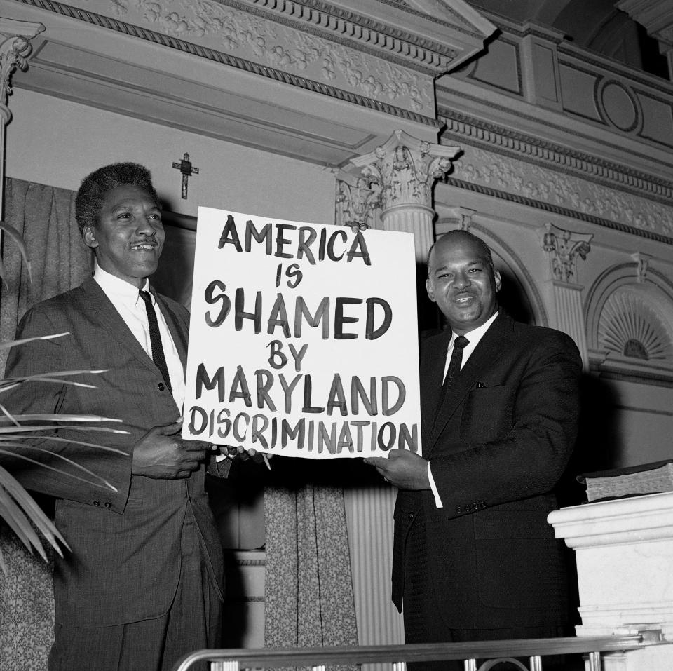 Bayard Rustin of New York City, left, and the Rev. Logan Kearse of Baltimore pose at Kearse's church, Cornerstone Baptist, with one of the signs carried by demonstrators who staged sit-ins on Nov. 18, 1961, at Baltimore restaurants in protest of segregation.