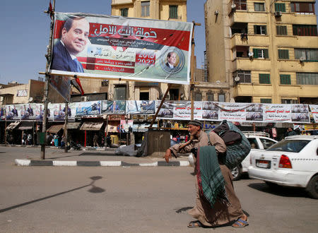 A street vendor selling clothes walks in front of banners of Egypt's President Abdel Fattah al-Sisi during preparations for the presidential election in Cairo, Egypt, March 25, 2018. REUTERS/Ammar Awad