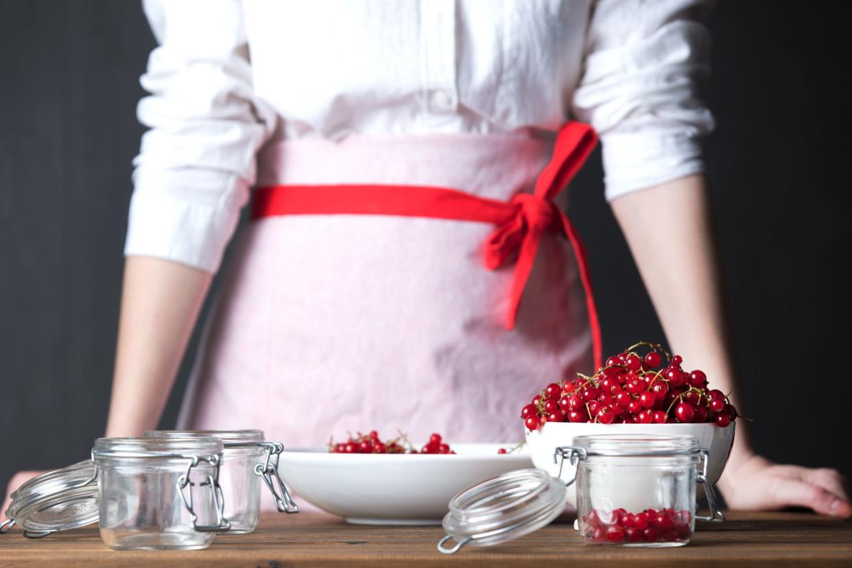 woman's torso standing over table with bowl, mason jars, and lingonberries