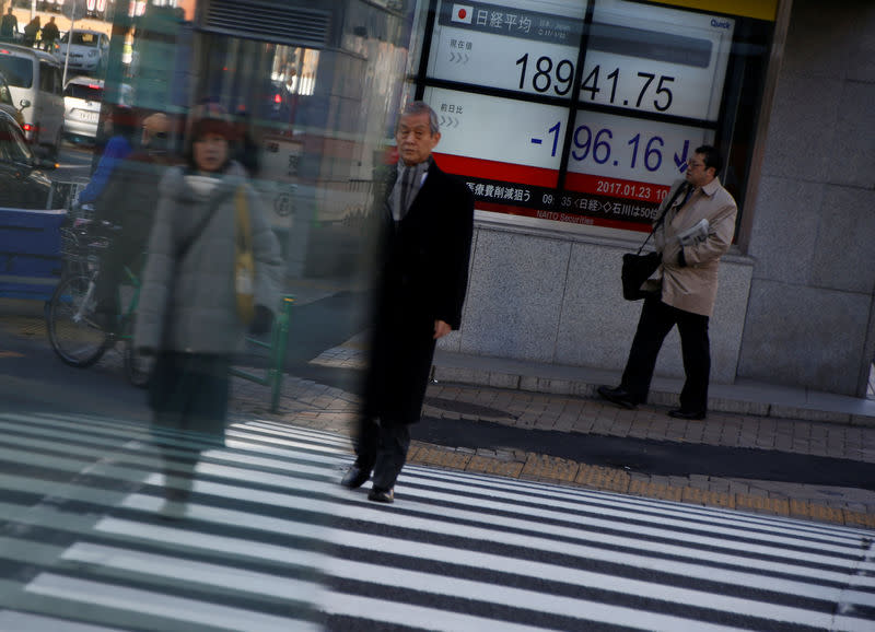 People walk past an electronic board showing stock prices outside a brokerage at a business district in Tokyo, Japan, January 23, 2017. REUTERS/Kim Kyung-Hoon