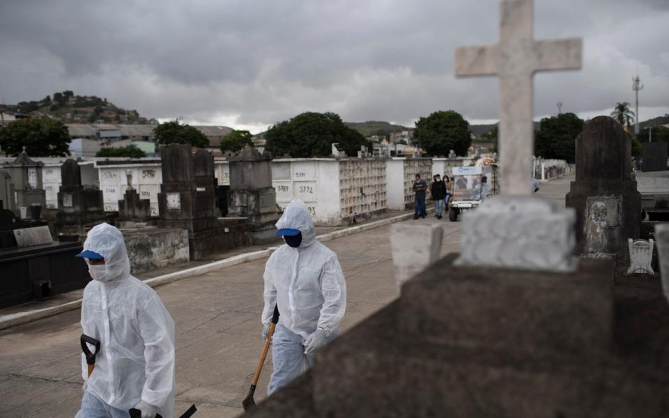 Cemetery workers in protective gear walk to the burial of a woman who died from complications related to Covid-19 - Silvia Izquierdo / AP