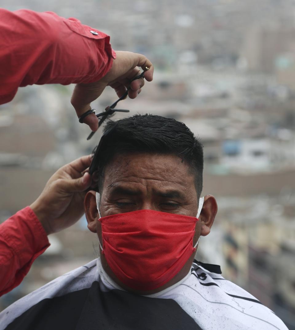Josue Yacahuanca clips the hair of a resident free of charge, at the top of a hill in the San Juan de Lurigancho neighborhood of Lima, Peru, Friday, June 19, 2020. Peru has roughly 150,000 barbers, but Yacahuanca is among a few who've decided to offer his services to those most in need. (AP Photo/Martin Mejia)