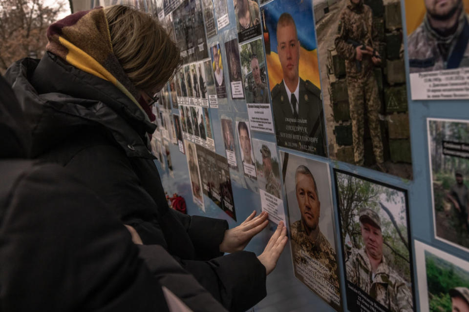 A woman attaches a photo to a memorial wall.