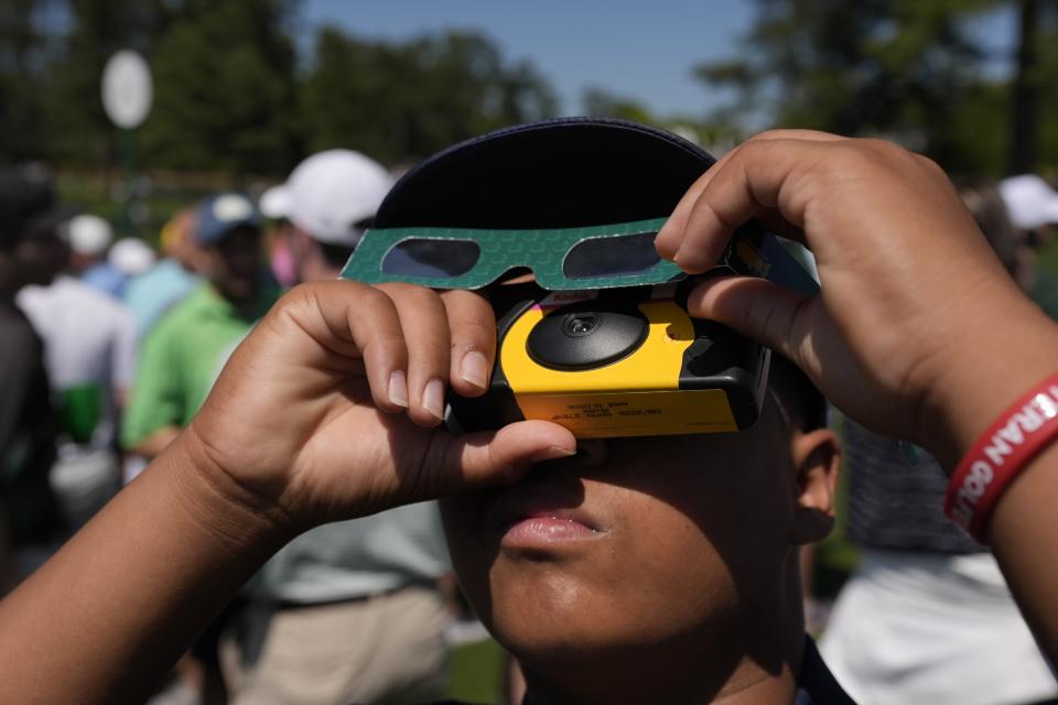 Xeve Perez looks up as the sun during an solar solar eclipse during a practice round in preparation for the Masters golf tournament at Augusta National Golf Club Monday, April 8, 2024, in Augusta, Ga. (AP Photo/George Walker IV)