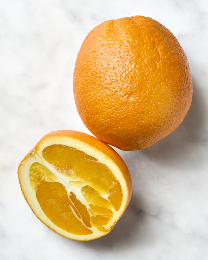 overhead shot of one whole and one half navel orange on a white marble surface.