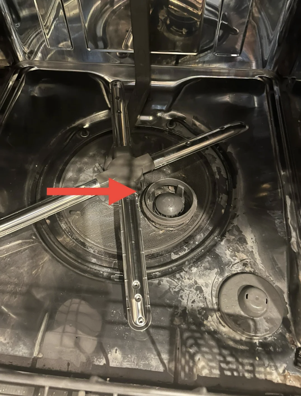 Close-up of a dishwasher interior showing a detached spray arm with a red arrow pointing to the issue