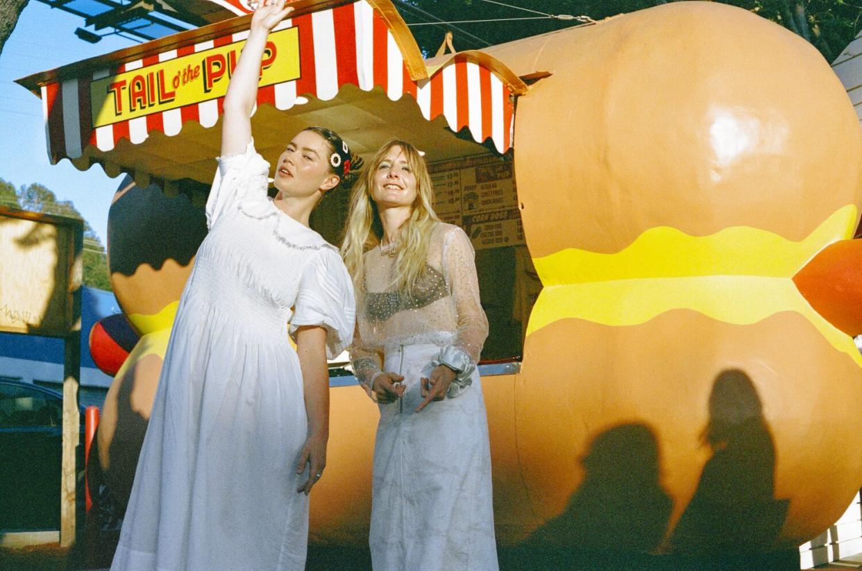 Two women stand in front of a hot dog stand.