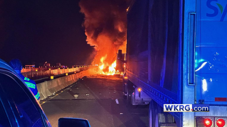 A photo of a car engulfed in flames in the early morning hours. To the right is an 18-wheeler and to the left is another car. The WKRG.com logo is in the bottom right corner.