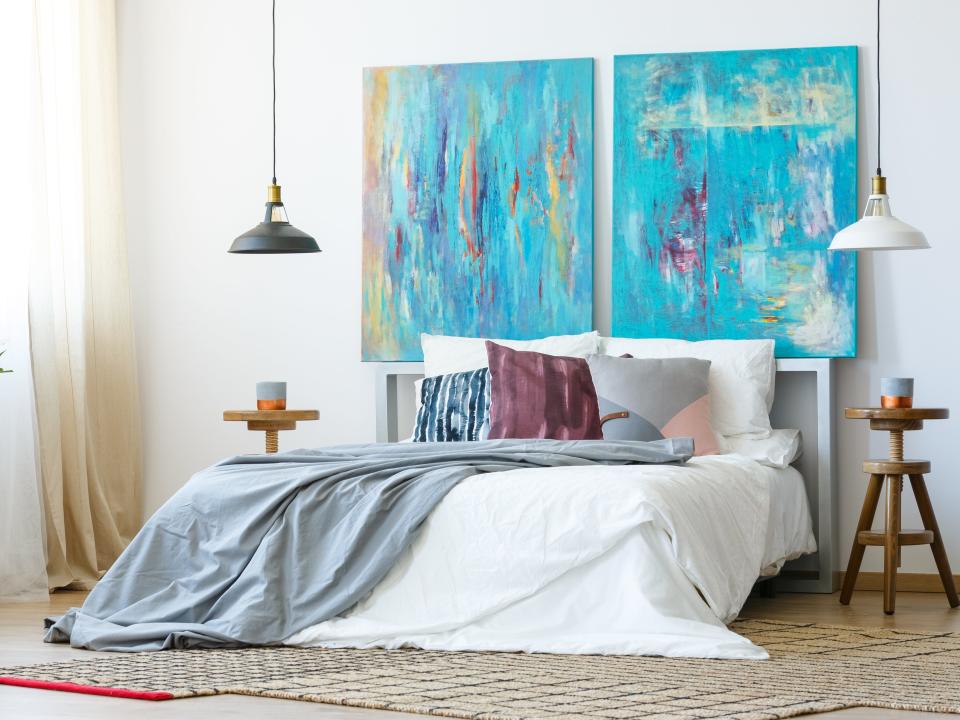 Bedroom with white bed with two large blue paintings over it and hanging lamps