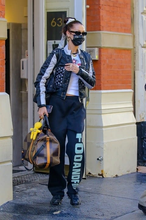 Bella in a studded jacket, a t-shirt and sweatpants carrying a duffle bag