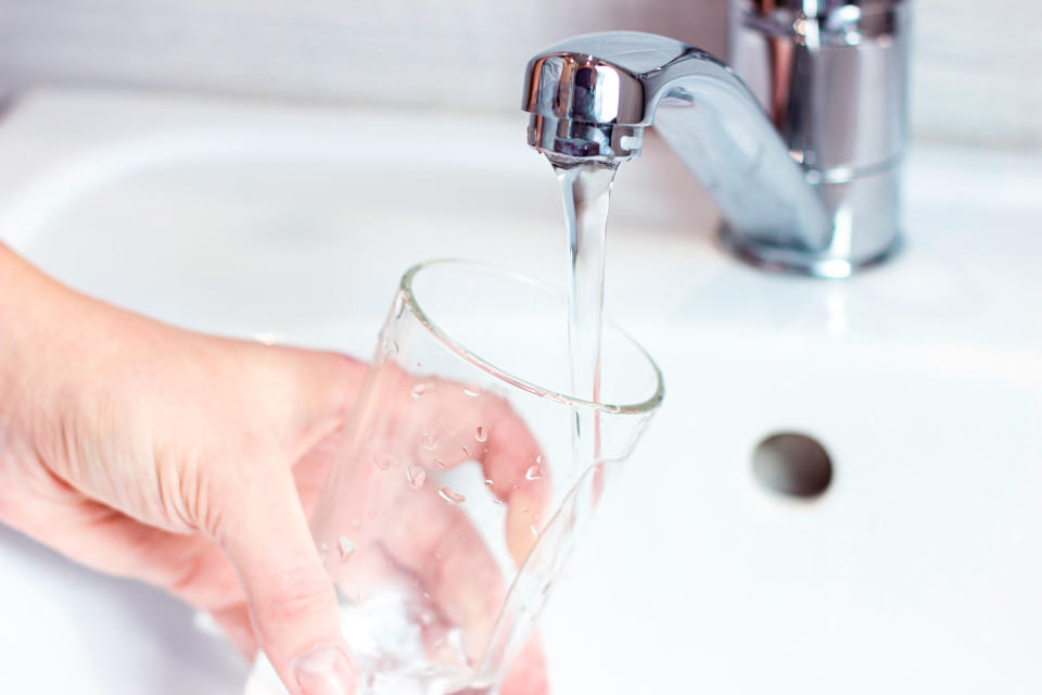 Young caucasian woman hand holding a glass with pure drinking water pouring from home faucet close up.