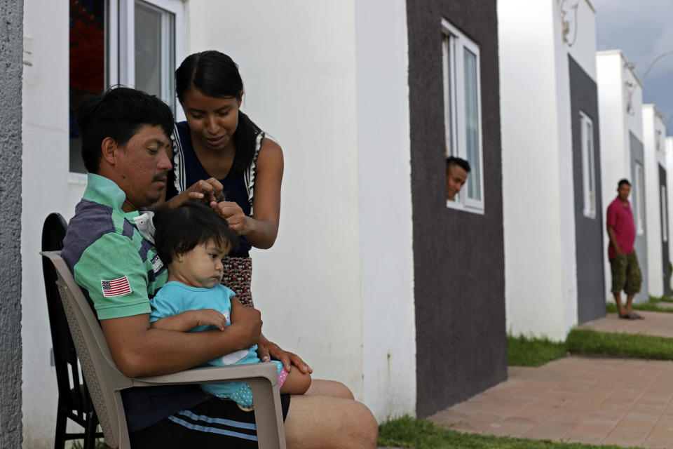 Elmer Erroa holds his daughter Ruth as his wife Lorena combs her hair, on the doorstep of their new government donated home, in the private development Ciudad Marsella, El Salvador, Tuesday, July 27, 2021. The Erroas, who were displaced by the October 2020 landslide triggered by a tropical storm, are among the families who were given a government-issued check in December for $25,300 to purchase the home in the middle-class community. (AP Photo/Salvador Melendez)