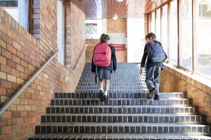 Two kids in uniform walk up a staircase.