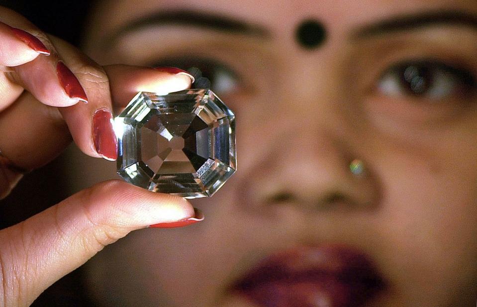 a woman, who is blurry in the background, holds a large diamond in her fingers in the foreground