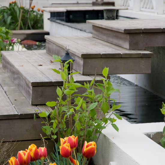 <p> Soften the hard edges of your decking with an abundance of pretty flowers and herbs that creep right up to the door. Floating steps made out of the same material as the decking create continuity between the two levels and add a note of fun by bridging the water feature below. </p>