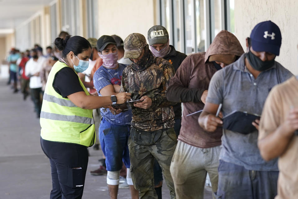 FILE - Cristela Martinez, left, helps people with their forms as they wait in line to receive the Johnson and Johnson COVID-19 vaccine at a clinic held by Healthcare Network, April 10, 2021, in Immokalee, Fla. The nation’s COVID-19 death toll stands at around 800,000 as the anniversary of the U.S. vaccine rollout arrives. A year ago it stood at 300,000. What might have been a time to celebrate a scientific achievement is fraught with discord and mourning. (AP Photo/Lynne Sladky, File)