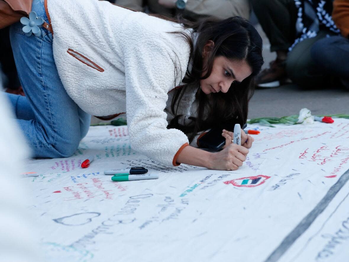 Lisha Almeida, a D.C.-area resident, writes a note on a memorial during a vigil for Aaron Bushnell, an active duty U.S. service member who died after setting himself on fire the day before in front of the Israeli Embassy in Washington, D.C. (Allison Bailey/Reuters - image credit)