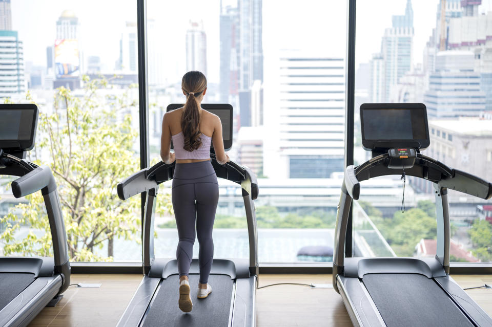 Rear View of Fitness Woman running on treadmill during a cardio session against city view in a health club.