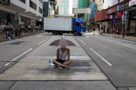 A protester sits under an umbrella as he attends a rally along a main street at Hong Kong's shopping district Tsim Sha Tsui October 1, 2014. REUTERS/Tyrone Siu