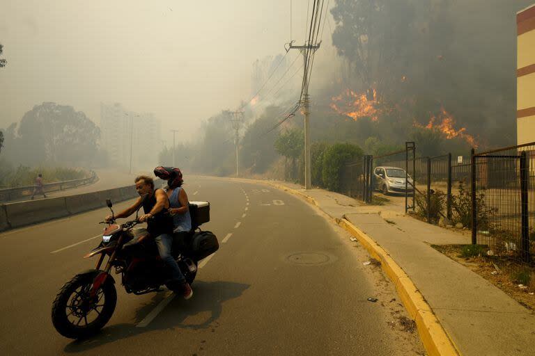 Residentes evacuan en una motocicleta mientras el humo causado por los incendios forestales llena el cielo y las llamas se extienden hacia Viña del Mar

