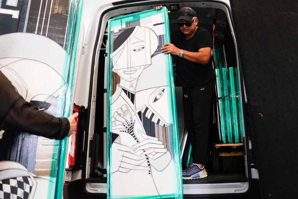 Julio Garcia, 64, of San Diego, California, hands pieces of artwork to his wife, Cecilia Garcia, 64, to prepare his booth at the Ann Arbor Art Fair in Ann Arbor on Wednesday, July 19, 2023. The 3-day fair features almost 1,000 artists and draws in close to half a million attendees each year.