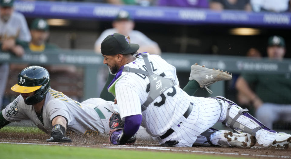 Oakland Athletics' Shea Langeliers, left, scores on a sacrifice bunt by Tony Kemp as Colorado Rockies catcher Elias Diaz falls while trying to collect the throw during the second inning of a baseball game Friday, July 28, 2023, in Denver. (AP Photo/David Zalubowski)