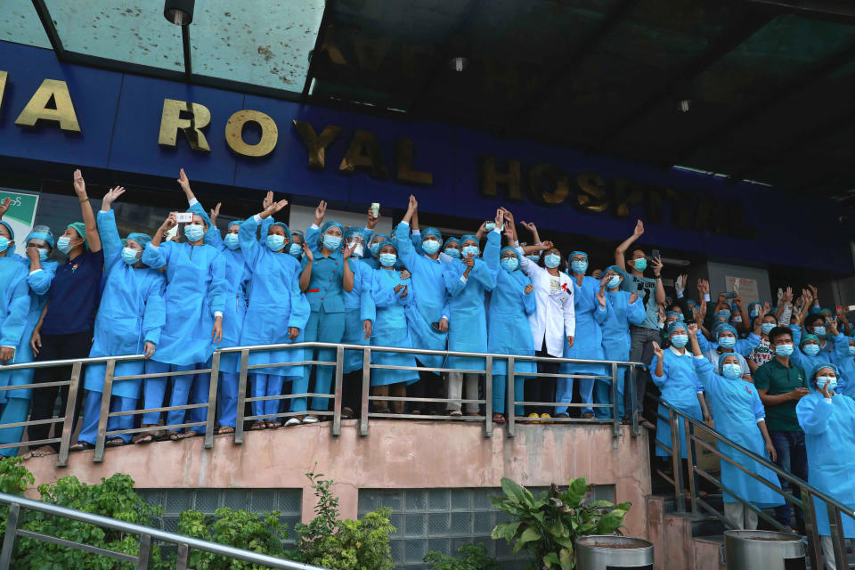 Staff wearing medical scrubs flash the three-fingered salute outside Asia Royal Hospital as they watch protesters march in Yangon, Myanmar on Sunday, Feb. 7, 2021. Thousands of people rallied against the military takeover in Myanmar's biggest city on Sunday and demanded the release of Aung San Suu Kyi, whose elected government was toppled by the army that also imposed an internet blackout. (AP Photo)