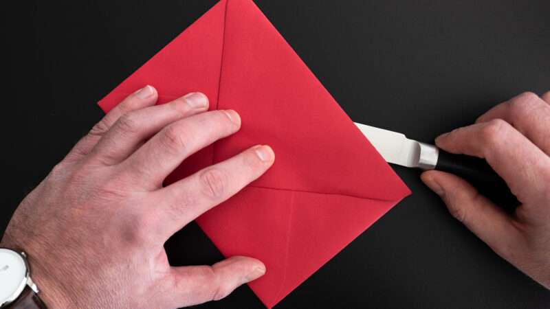 Close-up of a man's hands opening an envelope with a letter opener.