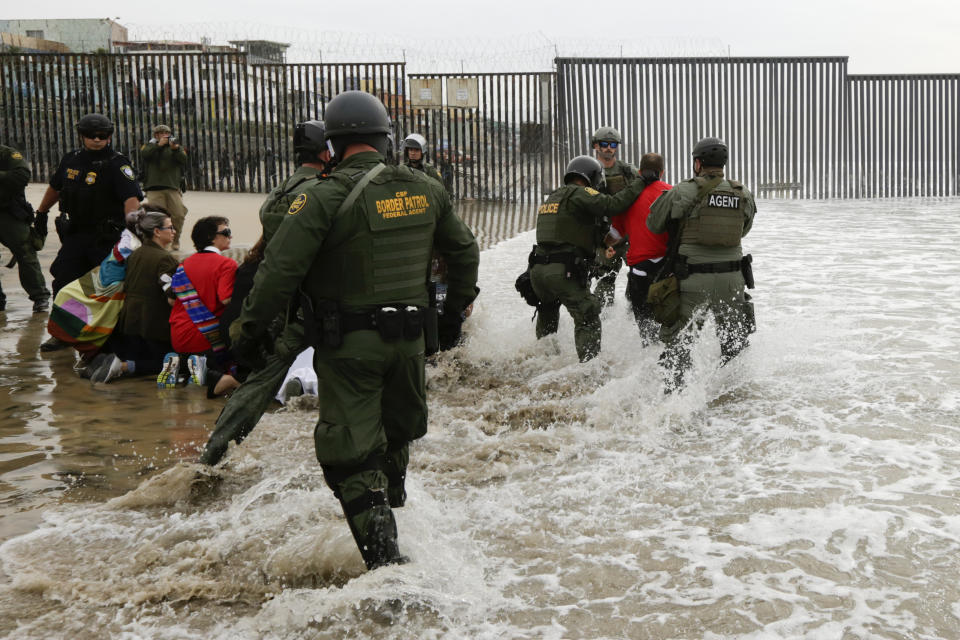 ARCHIVO - En esta foto de archivo del 10 de diciembre de 2018, agentes de la Patrulla Fronteriza, a la derecha, detienen a un hombre durante una protesta cerca de la frontera con Tijuana, México, en San Diego. La administración Trump ha cerrado silenciosamente el sistema de asilo de la nación por primera vez en décadas en medio de la preocupación por el nuevo coronavirus, en gran parte porque mantener a las personas bajo custodia se considera demasiado peligroso. (AP Foto/Gregory Bull, Archivo)