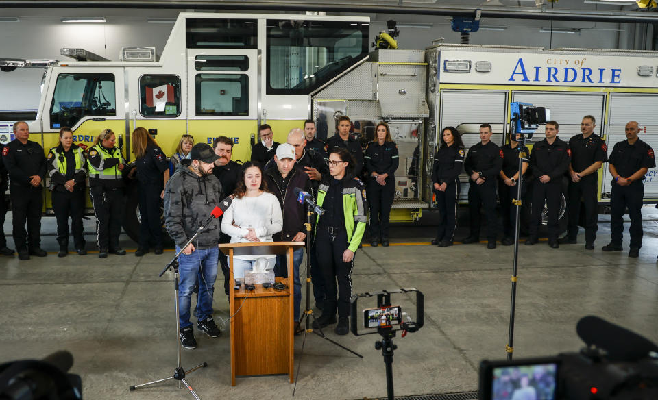 Paramedic Jayme Erickson, center, who was called to a crash last week and didn't know she was trying to save her own daughter because the injuries were too severe, is comforted by her husband Sean Erickson, center right, and friends as she speaks to the media in Airdrie, Alberta, Tuesday, Nov. 22, 2022. (Jeff McIntosh/The Canadian Press via AP)