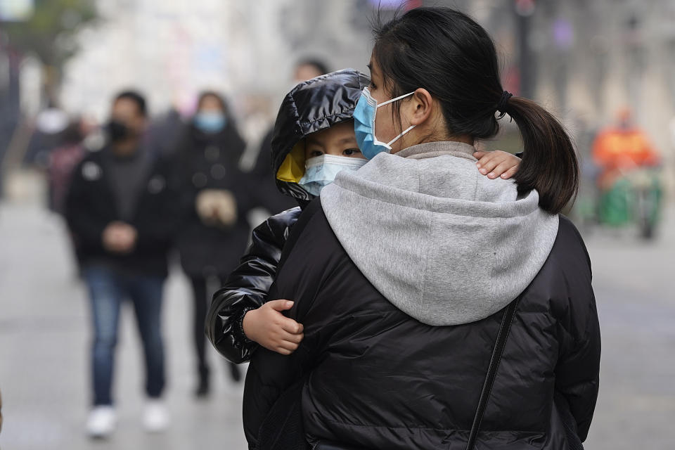 A child wearing a mask holds on to a woman as they walk through a popular shopping street in Wuhan in central China's Hubei province on Tuesday, Jan. 26, 2021. The central Chinese city of Wuhan, where the coronavirus was first detected, has largely returned to normal but is on heightened alert against a resurgence as China battles outbreaks elsewhere in the country. (AP Photo/Ng Han Guan)