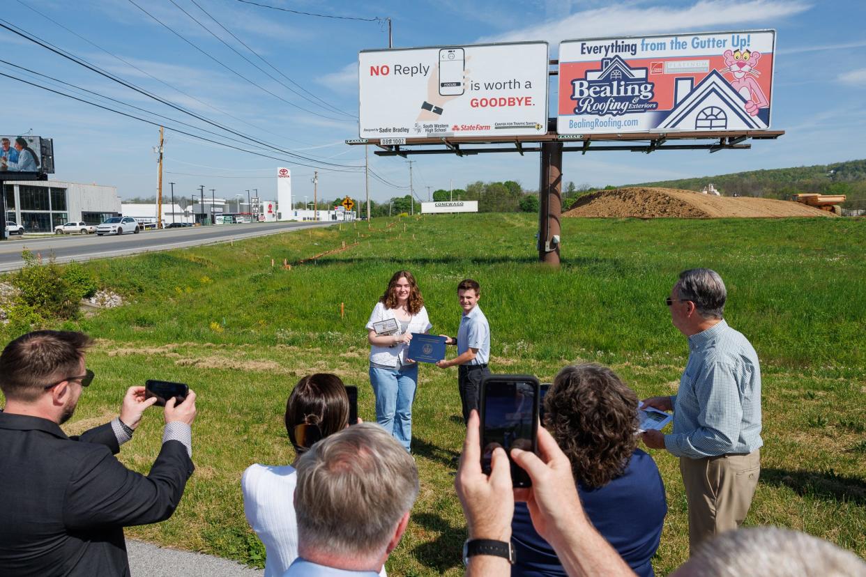Sadie Bradley, 10th grade student at South Western High School, poses for a photo while receiving a certificate of recognition from the office of Pa. representative Kate Klunk, as presented by Matthew Hutton, during an unveiling of her winning distracted driving billboard design along Carlisle Pike, Tuesday, April 30, 2024, in Hanover.