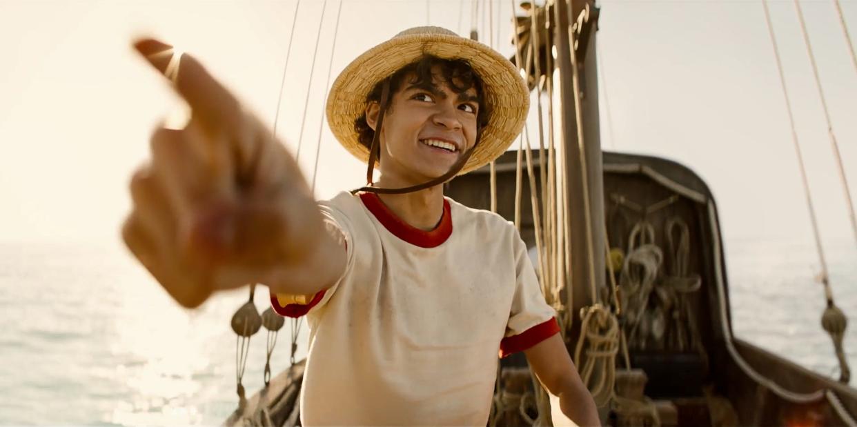 iñaki godoy as luffy in one piece, sitting on a boat and pointing forward with a smile on his face