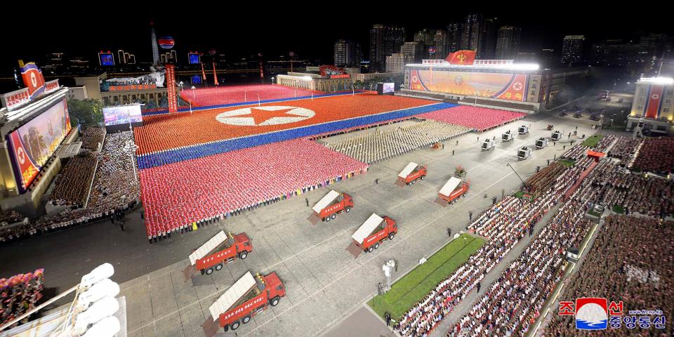 overhead shot of square featuring soldiers in colored uniforms forming the North Korean flag, while in foreground there are red box trucks with missiles emerging from their beds