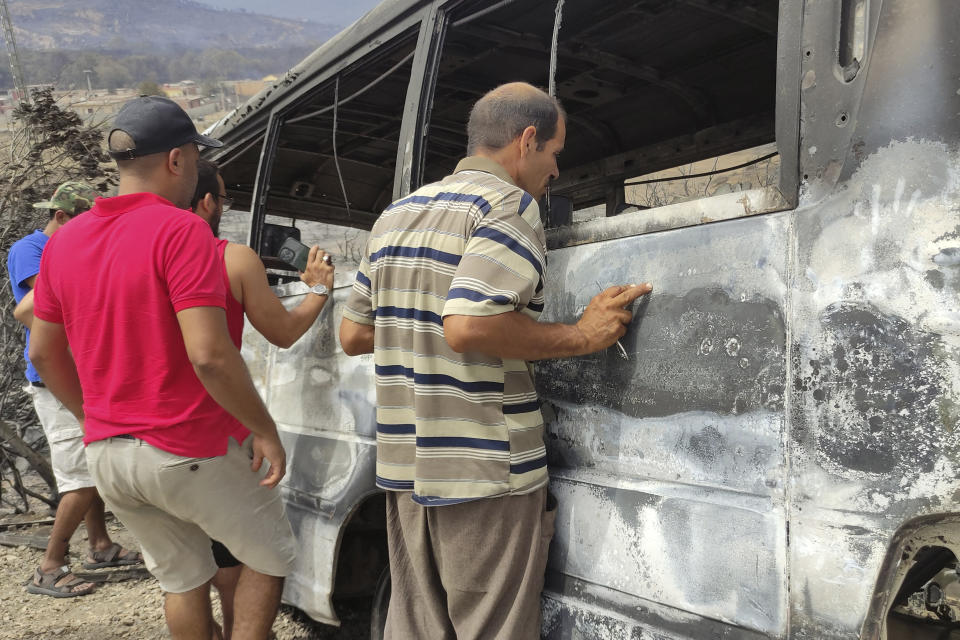 Men watch a charred van in a village of the region of El Tarf, near the northern Algerian-Tunisian border, Thursday, Aug.18, 2022. Wildfires raging in the forests of eastern Algeria have killed at least 26 people, according to a "provisional report" by the north African country's interior minister. (AP Photo/Mohamed Ali)