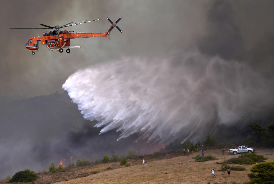 An helicopter drops water over a fire in Siderina village helicopter about 55 kilometers (34 miles) south of Athens, Greece, Monday, Aug. 16, 2021. Greek authorities have deployed dozens of firefighters, as well as six water-dropping planes and four aircraft to a wildfire that broke out Monday morning in the Keratea region southeast of Athens, near the national park of Sounion. (AP Photo/Thanassis Stavrakis)