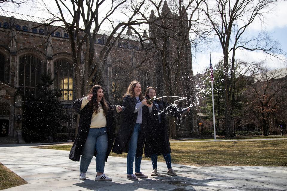 From left, graduating seniors Alex Andrews, Jenna Varcak and Haley Jamieson pop out a bottle of sparkling wine as they pose for a photo for their photographer Hannah Brauer  (not in the photo) in front of Law Library on University of Michigan main campus in Ann Arbor, Tuesday, March 17, 2020.