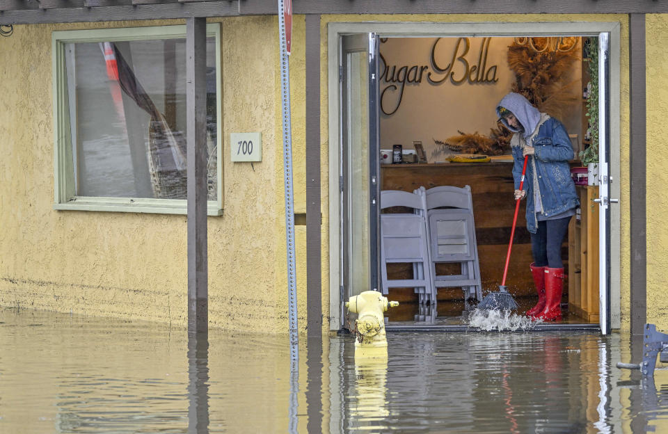 A worker at Sugar Bella sweeps flood waters out the front door on Marina Drive, just south of Pacific Coast Highway, Thursday, Feb. 1, 2024, in Seal Beach, Calif. (Jeff Gritchen/The Orange County Register via AP)