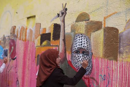 A Palestinian woman paints a mural, depicting a masked Palestinian holding a knife, in support of Palestinians committing stabbing attacks against Israelis, in Rafah in the southern Gaza Strip November 3, 2015. REUTERS/Ibraheem Abu Mustafa