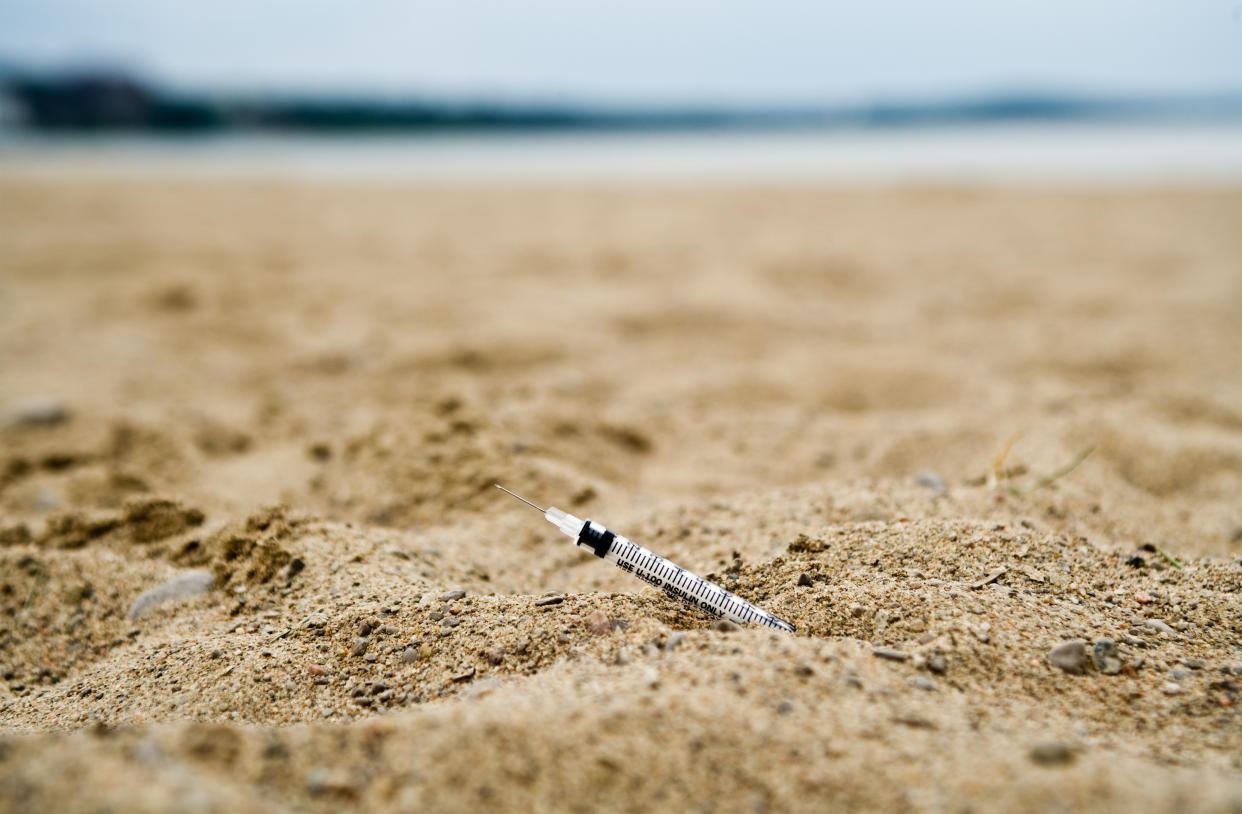 syringe sticking out of sand at a beach