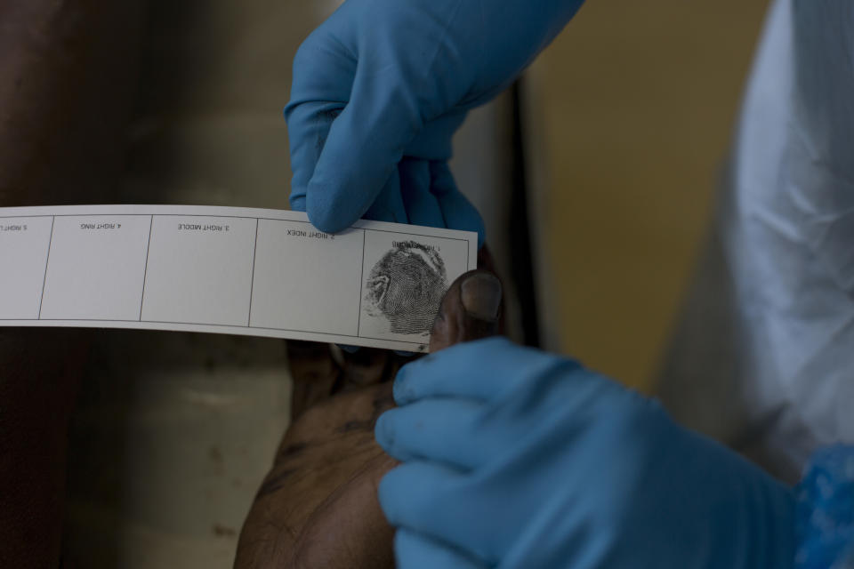 In this Wednesday, April 18, 2018 photo, a pathologist takes fingerprints of an unidentified male for forensic examination at a mortuary in the Hillbrow neighborhood of Johannesburg. Fingerprints are sent to a database of the South Africa police department in order to find a match. If no match is available, the bodies get buried in "pauper graves." (AP Photo/Bram Janssen)