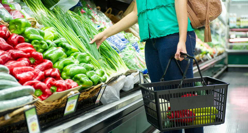 Supermarket shot showing woman reaching for fresh produce groceries in vegetable aisle.