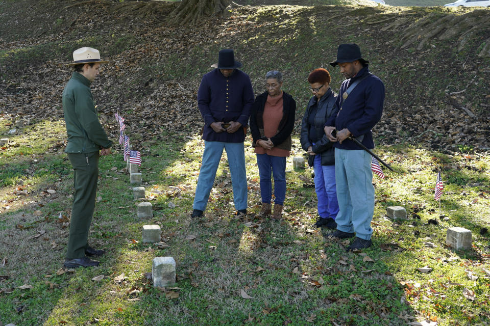 Vicksburg National Military Park Chief of Interpretation Brendan Wilson, left, conducts a ceremony of remembrance with two Civil War reenactors and Thelma Sims Dukes, center, and her niece Sara Sims at the burial site of 13 soldiers of the United States 1st Mississippi Infantry (African Descent) on Feb. 14, 2024, at Vicksburg National Cemetery in Vicksburg, Miss. The flags were placed at the graves of Black soldiers killed in an 1864 massacre at Ross Landing, Arkansas, who were buried as unknowns but have recently been identified. (AP Photo/Rogelio V. Solis)