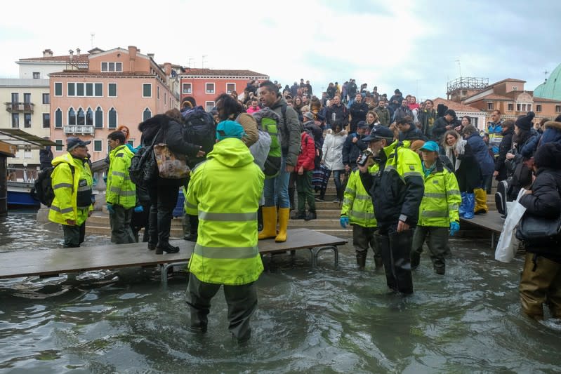 Tourist walk on the walkway in the flooded street during a period of seasonal high water in Venice