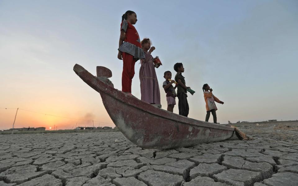 Children stand on a boat lying on the dried-up bed of Iraq's receding southern marshes of Chibayish in Dhi Qar province - ASAAD NIAZI /AFP