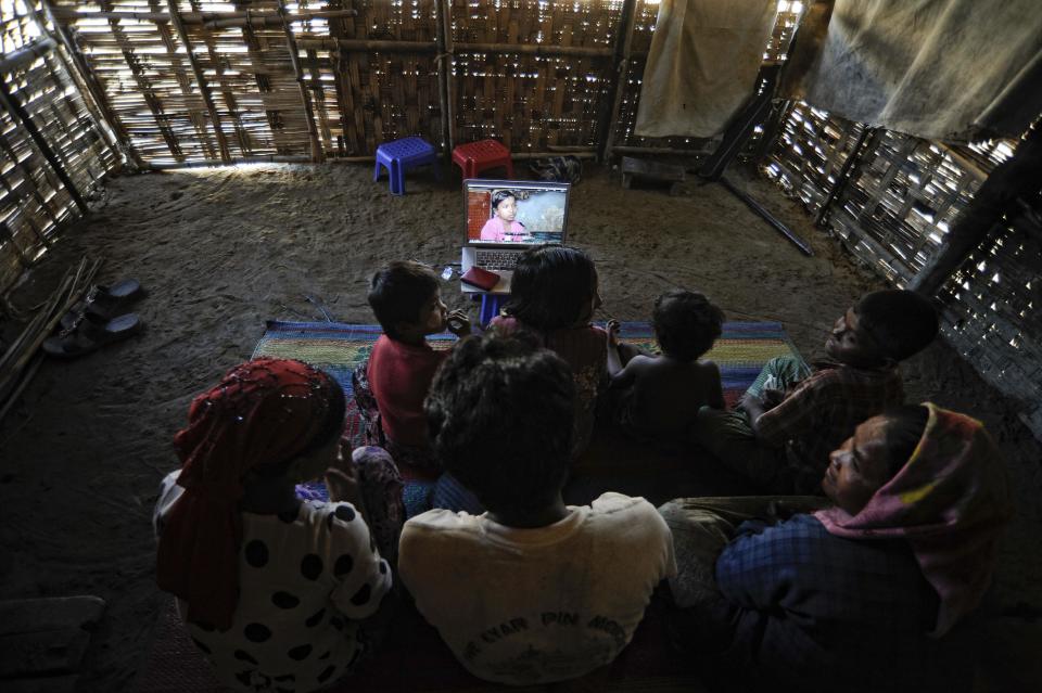 In this Nov. 29, 2013 photo, members of Senwara Begum's family watch her video interview at the Ohn Taw refugee camp on the outskirts of Sittwe, Myanmar. After their tiny Muslim village in Myanmar's northwest Rakhine had been destroyed in a fire set by an angry Buddhist mob, Senwara, 9, and brother, Mohamed, 15, became separated from the family. (AP Photo/Kaung Htet)