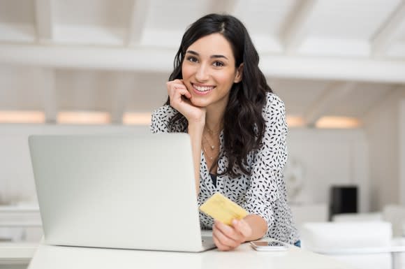 A smiling young woman holding a credit card and making an online purchase.