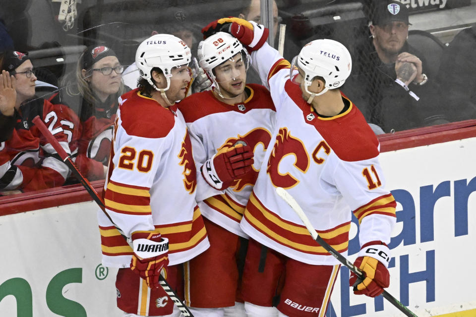 Calgary Flames left wing Andrew Mangiapane (88) celebrates his empty-net goal against the New Jersey Devils with Blake Coleman (20) and Mikael Backlund (11) during the third period of an NHL hockey Thursday, Feb. 8, 2024, in Newark, N.J. The Flames defeated the Devils 5-3. (AP Photo/Bill Kostroun)