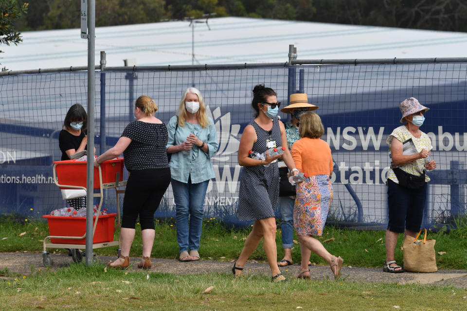 Hospital staff deliver water to people lining up for Covid-19 testing at Mona Vale Hospital's walk-in clinic.